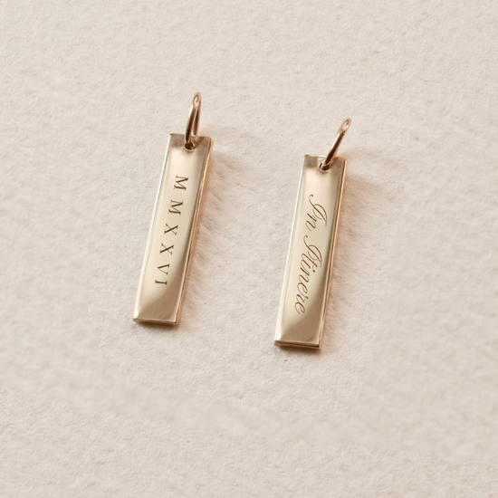 Gold bar pendants with engraved text on a light beige background