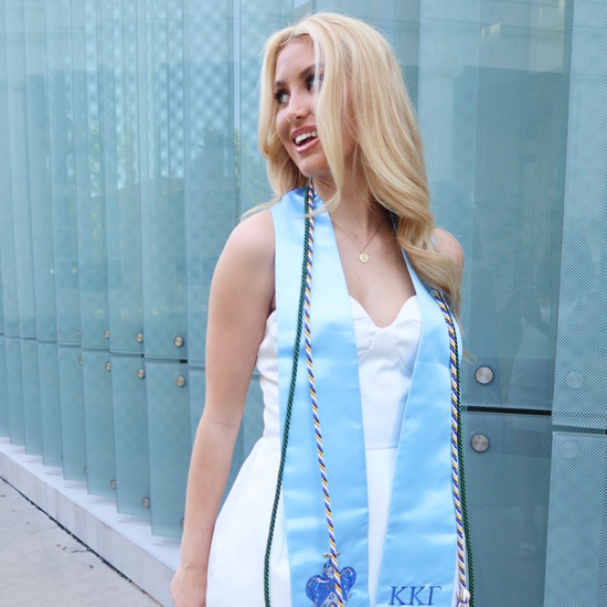 Woman wearing a white dress with a blue sky pattern and 'KKI' text, standing against a glass wall.