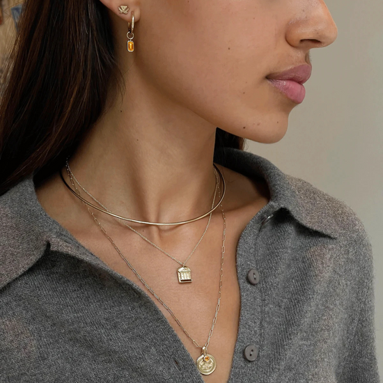 UVA Rotunda Pendant shown on figure in Cavan Gold on Cable Chain with UVA Sunburst Bundle in Cavan Gold, Neck Collar in Cavan Gold, and UVA V-Sabre Mini U Earring Bundle in Cavan Gold