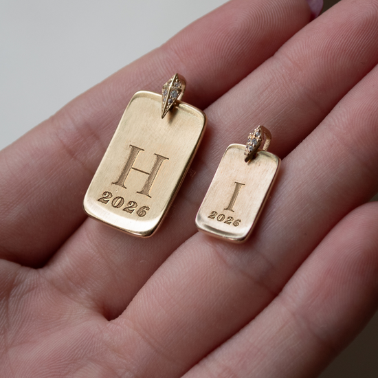 Gold pendants with 'H' and 'I' initials on a hand