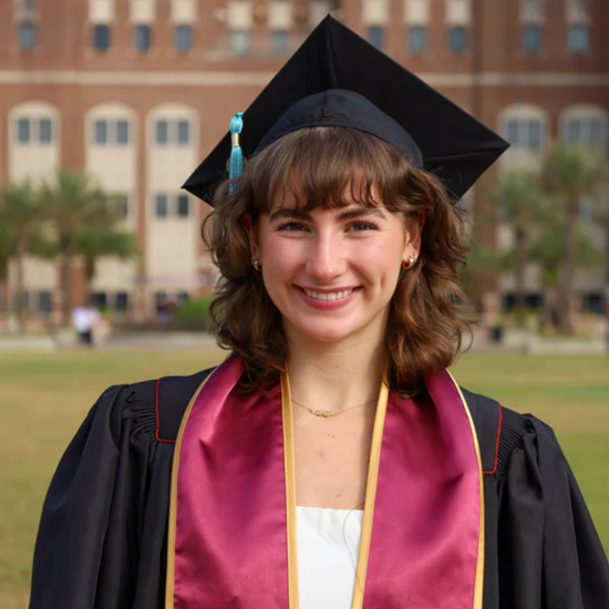 Graduate in cap and gown with a blurred background of a building and greenery