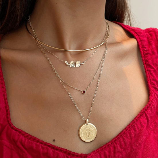 Close-up of a person wearing multiple gold necklaces with a red top.