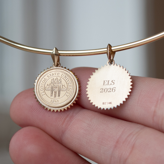 Gold bracelet with two engraved charms held by a hand against a neutral background