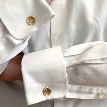 Close-up of a white dress shirt with a spread cuff and a gold-toned cufflink, worn on a person's arm.