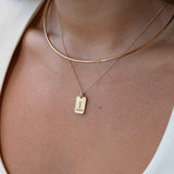Close-up of a person wearing a gold necklace with a tag pendant on a white background