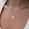 Close-up of a person wearing a gold necklace with a tag pendant on a white background