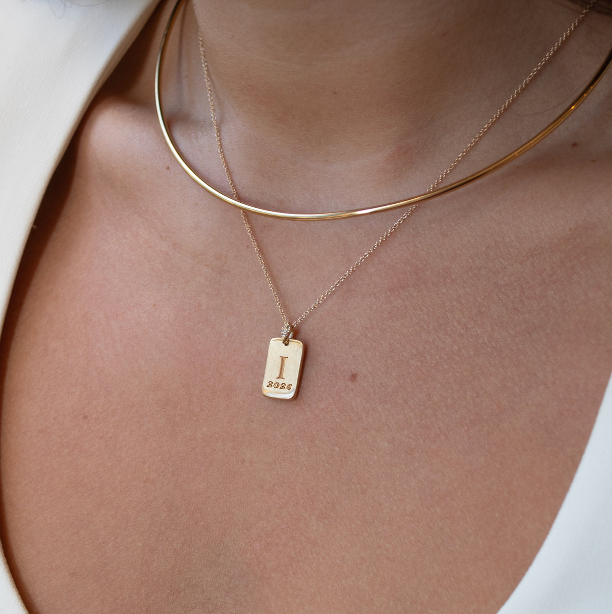 Close-up of a person wearing a gold necklace with a tag pendant on a white background