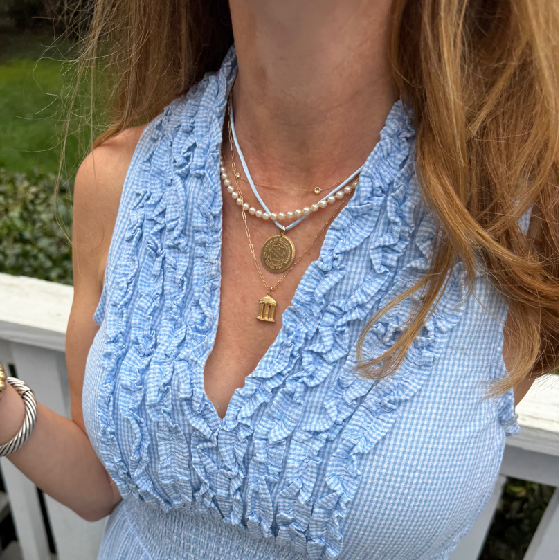 A woman wearing a light blue and white gingham smocked dress with a ruffled halter-style neckline, photographed outdoors on a wooden deck.