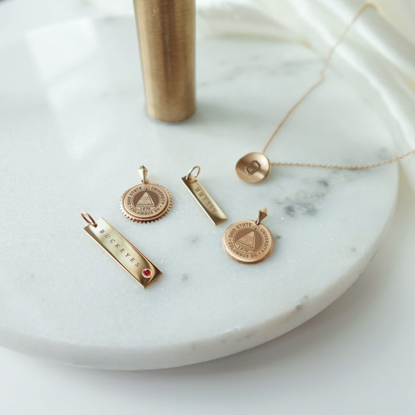 Ohio State collection featuring the Buckeyes Garnet Bar, Ohio State Sunburst, 2024 Bar, Ohio State Florentine, and Ohio State O Organic Necklace Petite laydown shown in gold