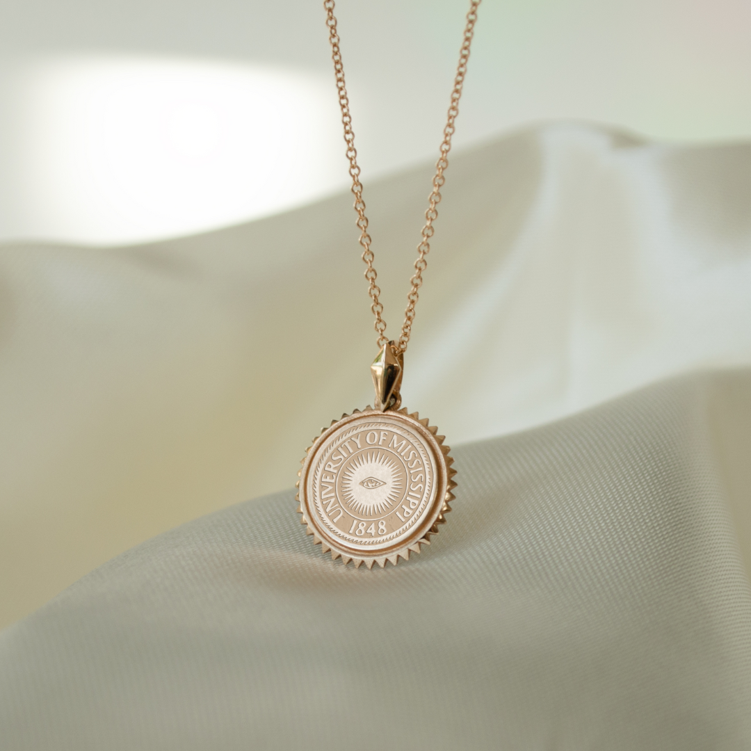Ole Miss Eye Seal Sunburst Pendant shown in Cavan Gold with Cable Chain and silk background