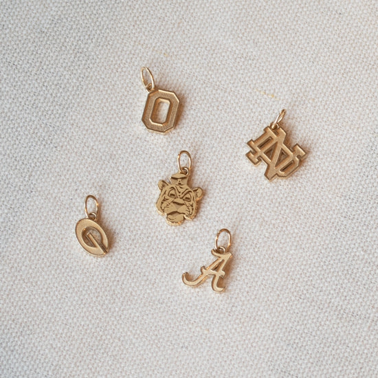 Set of gold charms including letters and a face on a light gray background
