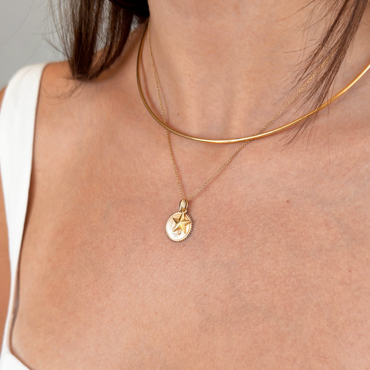 Gold necklace with a pendant on a person wearing a white top against a neutral background