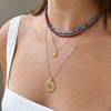 Close-up of a person wearing multiple necklaces with a focus on a gold coin pendant.