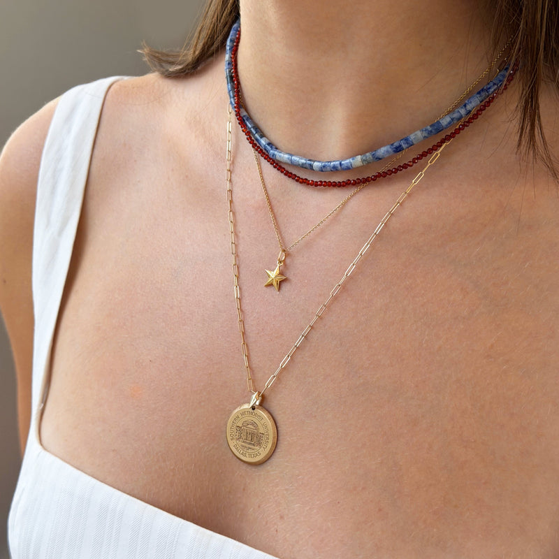 Close-up of a person wearing multiple necklaces with a focus on a gold coin pendant.