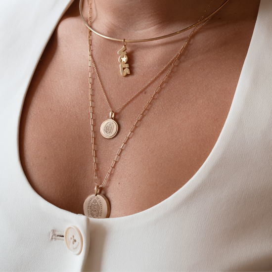 Close-up of a person wearing multiple gold necklaces with pendants on a plain background