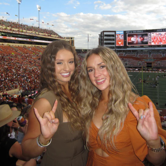 Two women posing for a photo at a sports event with a large stadium in the background.