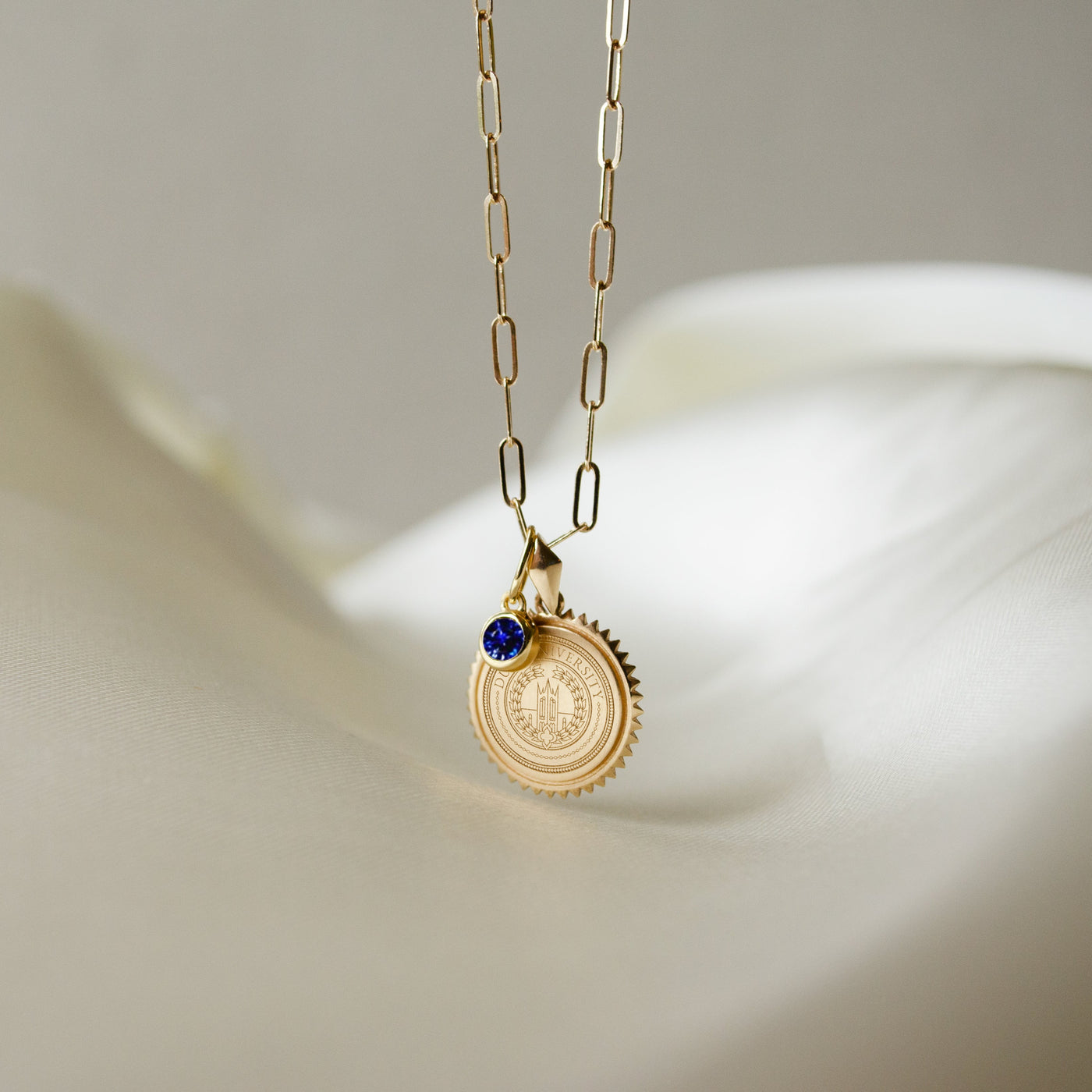 Duke University Seal Sunburst shown as a Sunburst Bundle on Link Chain with Sapphire Gemstone Charm in gold